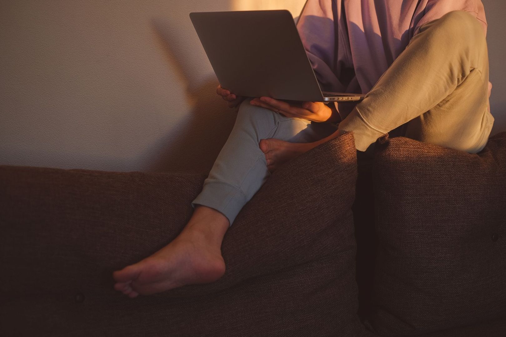 Person med laptop i soffan under en varm kvällsbelysning