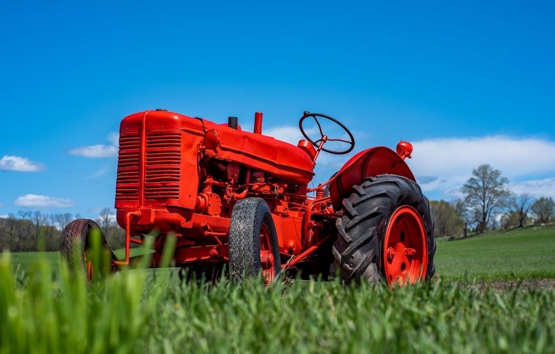 Röd äldre traktor står på ett grönt fält under klarblå himmel