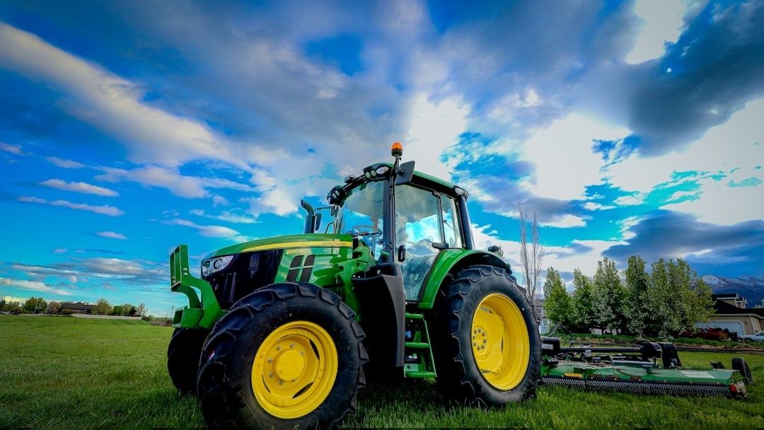 Grön traktor med gula hjul och klippaggregat på en gräsåker